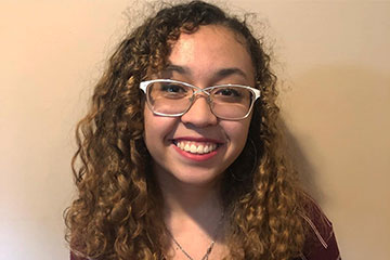 Lauren Williams, an OSU student wearing a striped shirt and eyeglasses, smiles for a portrait photo.